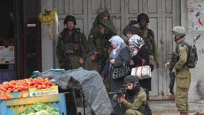 Palestinian women walk past Israeli security forces during clashes with Palestinian stone throwers in the West Bank city of Hebron. Hazem Bader / AFP