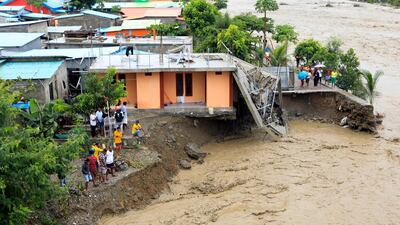 People stand near a damaged house hit by flood water on a river bank in Dili, East Timor. Dozens of people are dead or missing as floods and landslides caused by torrential rains hit the eastern part of Indonesia and East Timor. EPA