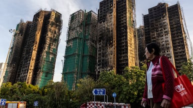 A woman walks past the charred remains of the high-rises in Hong Kong's Tai Po district. Getty Images