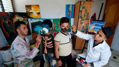 Palestinian artists Hammam Mosallam (L) and Yussef Abu Zerr (R) apply facepaint on a mask and a child's face at their home workshop in the Nusseirat refugee camp in the central Gaza Strip. AFP