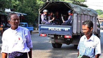 A riot police car drive past near the National League for Democracy headquarters (NLD) as two party members stands outside.