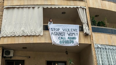 epa08366817 A woman hangs a sign on her balcony with phrases protesting domestic violence against women in Beirut, Lebanon, on April 16, 2020. The protest is organizing by ABAAD, a non-profit, non-politically affiliated, non-religious civil association that aims to achieve gender equality as an essential condition to sustainable social and economic development in the MENA region. EPA