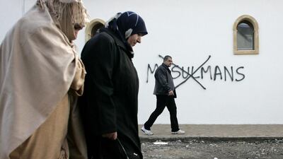 Muslim residents in France walk past racial slurs painted on the walls of a mosque in the town of Saint-Etienne. Laurent Cipriani / AP