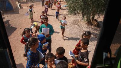 Displaced Syrian children queue for their turn outside a bus converted into a classroom.