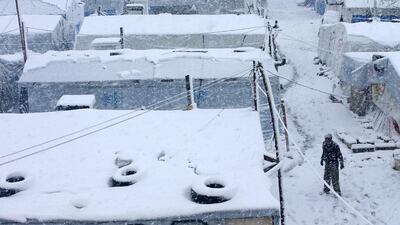 A Syrian man, right, walks between tents covered in snow. Hussein Malla / AP Photo