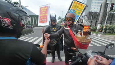 People wearing character clothes of local hero Gundala (right) and Batman (left) offer Indonesian traditional herbal drinks “Jamu” to motorists as they encourage them to stay healthy and fight COVID-19 in Solo, Indonesia. AFP