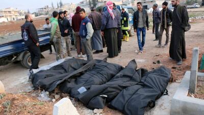 Syrians stand near the bodies of civilians killed in air strikes on Khan Sheikhoun in Idlib province on December 17, 2017. Syrian Civil Defense White Helmets via AP