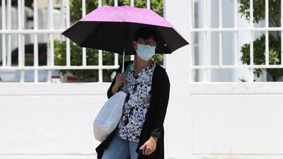A commuter walks to the bus stop with an umbrella in Jumeriah, Dubai. Chris Whiteoak / The National