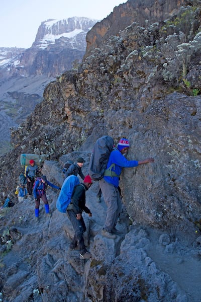 A group of trekkers inches around the so-called Kissing Rock on the tricky Barranco Wall section of trail on Mt Kilimanjaro. Getty Images