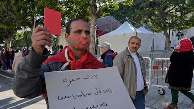 A Tunisian protester holds a red card as he holds a placard with a slogan criticising politicians in his country during a rally marking the ninth anniversary of the 2011 uprising, at Habib Bourguiba Avenue in Tunis on January 14, 2020. AFP