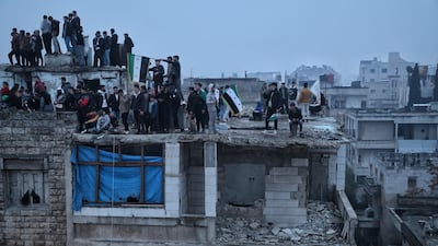 People stand on the roof of a partially damaged building during a parade marking the first anniversary of the ousting of the Bashar al-Assad regime in Idlib, Syria, 08 December 2025. Syria marks the first anniversary of the overthrow of the Assad regime on 08 December when the dictatorship of Bashar al-Assad collapsed during a major offensive by opposition forces. EPA / BILAL AL-HAMMOUD