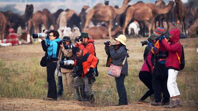 A group of tourists point their cameras as they photograph camels and their handlers at the camel fair grounds in the outskirts of Pushkar. Roberto Schmidt / AFP