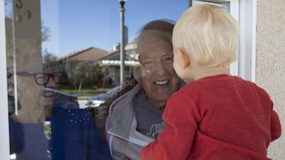 A child in California greets his elderly neighbour through a window, adhering to social distancing rules, on April 3, 2020. AFP