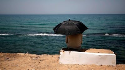 A Palestinian sits beneath an umbrella by the shoreline of a beach in Gaza City. AFP