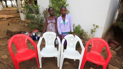 Sisters Diamond, right, and Secret Moore pose for a family portrait at their home in the Pipeline Community outside Monrovia, Liberia. The empty chairs represent their mother, father, grandmother and aunt who died of the Ebola virus during an outbreak of the disease in 2014. Ahmed Jallanzo / EPA