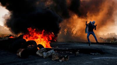 A Palestinian uses a slingshot to hurl stones amid smoke during clashes with Israeli troops in Ramallah. AFP