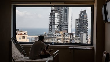 The Beirut port is seen through a smashed window as a man takes a break from cleaning debris from the heavily damaged St George Hospital on August 13, 2020. Getty Images
