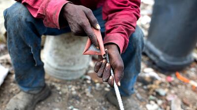 Mr Aristide, a 36-year-old trash scavenger, uses sand paper to smoothen the metal rod he uses to pick through the rubble. AP Photo