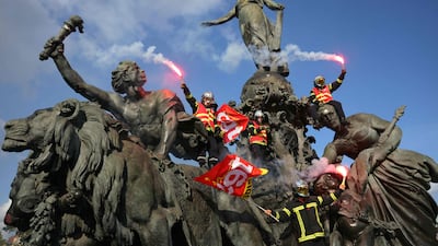 Firefighters wave flares as they climb on The Triumph of the Republic statue at Place de la Nation in Paris, during a rally to demand additional resources after a summer of record wildfires. AFP