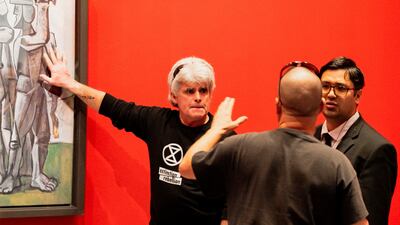 A climate activist stands with a hand glued to the perspex covering of Picasso's work 'Massacre in Korea'. Matt Hrkac/ Reuters