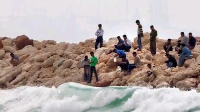 Men walk near the beach at Ajman as waves batter the rocks.