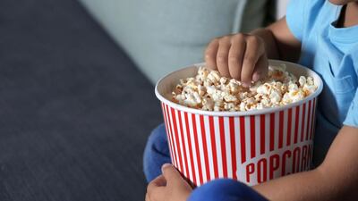 Stock image: A child eating popcorn while watching TV. Alamy