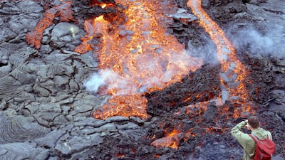 A man takes a picture as lava flows from the volcano. Now officially named Fagradalshraun, or 'beautiful valley of lava' after the nearby Mount Fagradalsfjall, the volcano rose up from a fissure in the ground. AFP