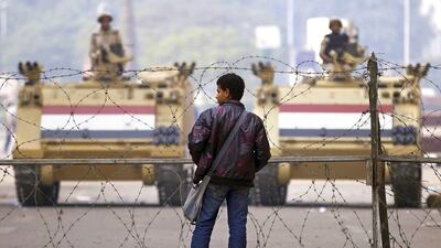 A man stands in front of a barbed wire fence set up by soldiers standing guard on armoured personnel carriers near Tahrir Square in Cairo. Gulf states have shovelled billions of dollars towards the governments of neighbouring Arab states. Amr Abdallah Dalsh / Reuters