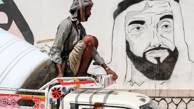 A Yemeni man riding on top of a pick-up truck driving past a mural depicting the UAE's Founding Father Sheikh Zayed in Mukalla. AFP