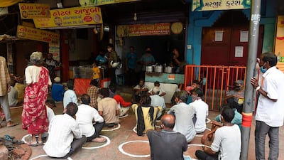 People in need sit while maintaining social distancing in front of a restaurant offering free meals in Ahmedabad. AFP