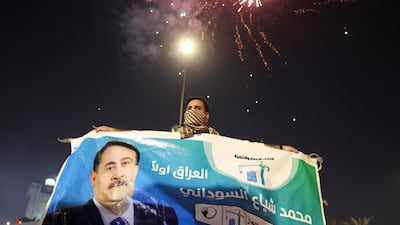 A man holds an election poster featuring current Prime Minister Mohammed Shia Al Sudani, with fireworks in the background, as his supporters celebrate after preliminary result was announced in Baghdad, on November 12. Reuters