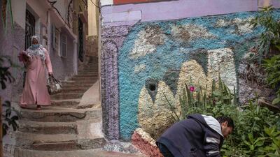 A man paints outside his home while a woman wearing a face mask walks past during a health state of emergency and home confinement order in Rabat, Morocco. AP Photo