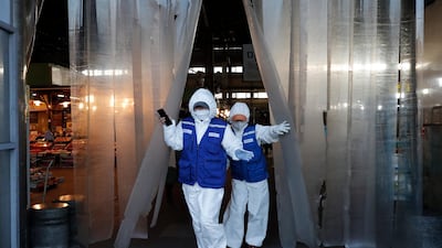 Workers wearing protective suits walk before they spray disinfectant as a precaution against the COVID-19 at a market in Seoul, South Korea, AP