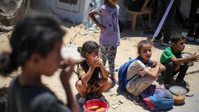 Palestinian children sit on the ground with cooked meals they received at a distribution point in Nuseirat, in the central Gaza Strip. AFP