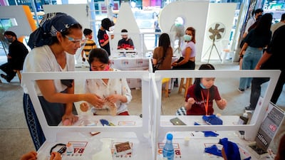 People are separated by plastic partitions to ensure minimum social distancing as they make protective face masks for children with cloth at a fair in Bangkok, Thailand. EPA