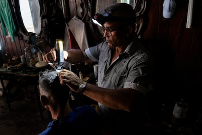 A hairdresser works by the light from a headlamp in Matanzas, Cuba. AFP
