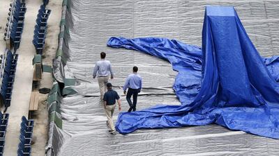 Men walk on the tarp-covered court in Arthur Ashe Stadium after the women's semi-final matches were postponed on Thursday. Kathy Willens / AP