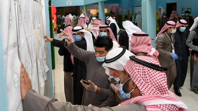 People wearing protective masks searches for her name on a voter list at a polling station in Kuwait City. EPA