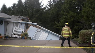 A Newport Firefighter looks at a home that was damaged from storms in Newport, Oregon. Fresh storms barreled through the already sodden Pacific Northwest, triggering a landslide that killed a woman near the Oregon Coast and clogging mountain passes in the Washington Cascades. Steve Card / Newport News-Times via AP