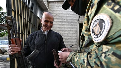 A Hayat Tahrir Al Sham guard collects the weapon of a former security guard at the Baath party offices in Damascus