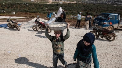 Displaced Syrian children carry their family's belongings as they arrive at a newly built camp near the town of Atmeh in Idlib. Getty