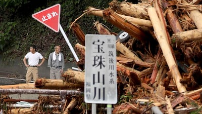 Local residents stand beside drifted wood and a damaged road sign following heavy flooding in Asakura, Fukuoka prefecture on July 8, 2017. The death toll from heavy rains and flooding in southern Japan has risen to 15, media reported, as rescuers continued work to bring out isolated survivors. JAPAN OUT / AFP PHOTO / JIJI PRESS / STR / Japan OUT