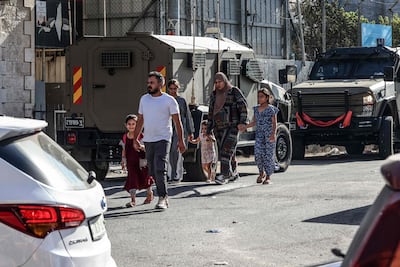 Palestinians walk past Israeli security forces deployed on a street during a military raid in the Qalandiya refugee camp. AFP