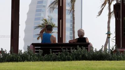 People wearing protective face mask as a preventive measure against the spread of coronavirus and maintaining safe distance when sitting on the benches at the Umm Suqeim park near Burj Al Arab hotel in Dubai. Pawan Singh / The National