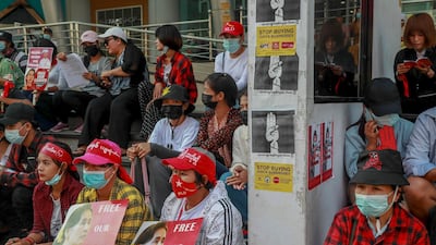 Protesters sitting next to signs to boycott Myanmar military-linked business, display pictures of deposed Myanmar leader Aung San Suu Kyi in Yangon, Myanmar on Tuesday, Feb. 23, 2021. AP