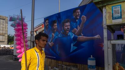 A cotton candy seller walks past a poster outside the Narendra Modi Stadium. AP