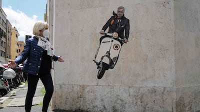 A woman walks past a mural depicting the new coach of AS Roma, Jose Mourinho, riding a scooter bike, on a wall of a building in the Testaccio district of Rome.
