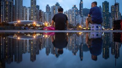 Fishermen are reflected in a puddle as Hong Kong's skyline looks in front of them. Despite a contracting economy, existing house prices in Hong Kong have risen 1.2 per cent this year, according to Centaline. EPA