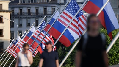 People walk under Russian and American flags on a bridge in the city center of Geneva. Getty Images