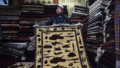 An Afghan carpet trader displays a rug showing different weapons and machinery as he waits for customers at his shop on Chicken Street, Kabul. More than three decades of war have damaged Afghanistan's once-thriving carpet industry, but weavers are tapping into the bloody past to boost their fortunes. AFP PHOTO
